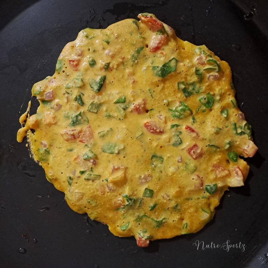 An image of half-cooked cheela on a griddle.